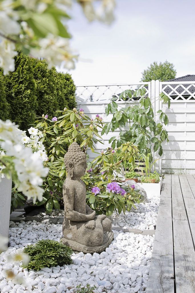 Terrassen ligger på bakkeplan med direkte utgang fra stuen. Hvite steiner, grønne planter og jernmøbler sender tankene mot varmere strøk.